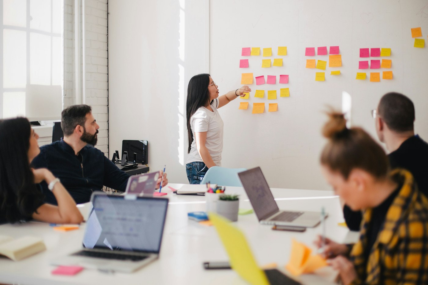 A team gathered around a table, listening as a colleague shares ideas on a wall of sticky notes.