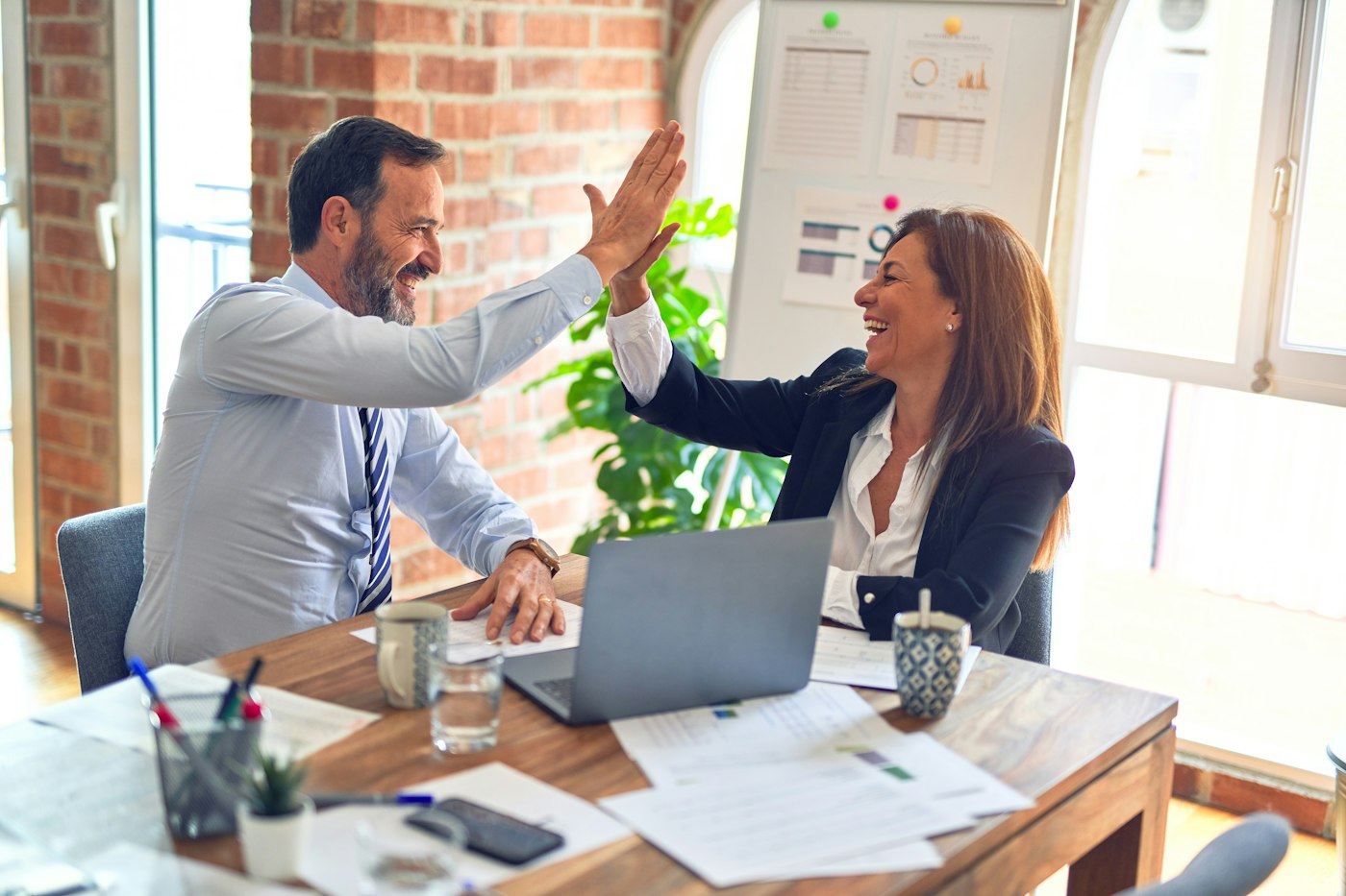 Two colleagues at a meeting table share a warm, joyful moment of connection.