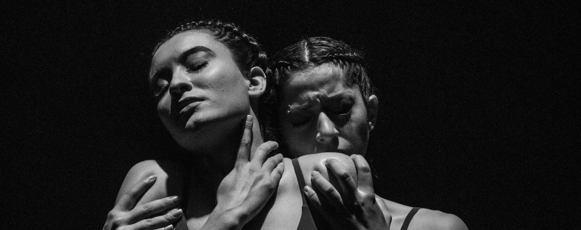 Two women in a dramatic, intertwined pose against a dark background — photograph by Anderson Portella